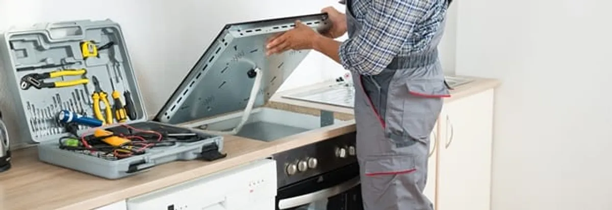 Cooktop repair technician lifting a built-in stovetop for service in Providence, RI